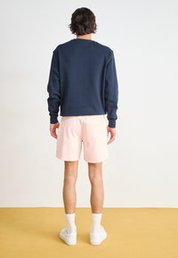 Marineblå crewneck sweatshirt, lyserøde shorts og hvide sneakers med ribbede hvide strømper. Glat stof, afslappet design, bagansigt.