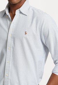 Light blue and white striped long-sleeve shirt with a button-down collar and a small embroidered polo logo on the chest. Cotton fabric.