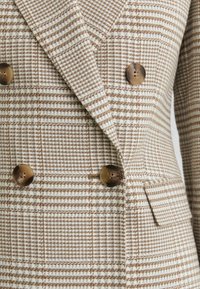 Beige en bruin geruit colbert met een dubbelzijdig ontwerp en vier bruine knopen, voorzien van brede revers en een klepzak aan de voorkant.