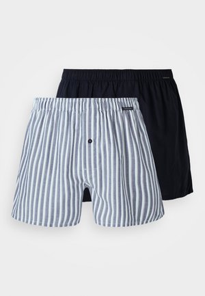 Deux paires de boxers pour hommes : l'une est marine, et l'autre est à rayures verticales bleues et blanches. Les deux comportent des ceintures élastiques et un détail de bouton à l'avant.