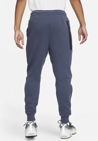 Marina joggers med tapered passform, elastisk midjeband och sidofickor med dragkedja. Tillverkade av mjukt tyg med en slät yta, parat med sportskor.