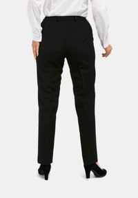 Zwarte, op maat gemaakte broeken met een slim fit, met een gladde textuur, riemlussen en een middelhoge taille. Gekleed met een wit shirt en zwarte hakken.