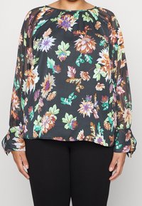 Blomsterbluse med sort gennemsigtig stof, prydet med livlige flerfarvede blomster og blade, lange ærmer og en sammensyning ved halsudskæringen.