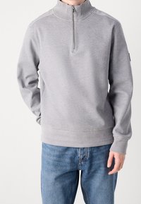 Gray textured sweatshirt with a high collar and zip closure, featuring ribbed cuffs and hem, paired with blue denim jeans.