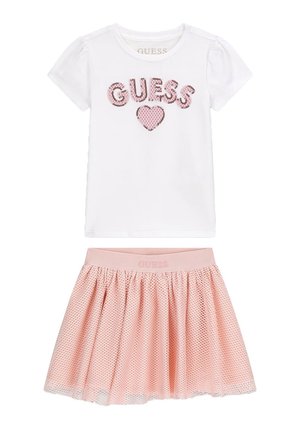 Camicia bianca a maniche corte con "GUESS" e cuore rosa di paillettes, abbinata a gonna rosa in tessuto mesh con fascia elastica in vita.