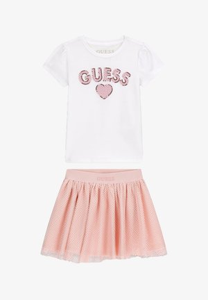 Camicia bianca a maniche corte con "GUESS" e cuore rosa di paillettes, abbinata a gonna rosa in tessuto mesh con fascia elastica in vita.