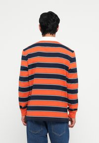 Camisa polo de manga longa com riscas horizontais laranja e azul-marinho em destaque, feita de algodão, com colarinho clássico e punhos canelados.