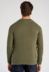 Olivengroene gebreide trui met geribde ronde hals en manchetten, lange mouwen en een losse pasvorm. Heeft een gestructureerde stof en zijsplitten.