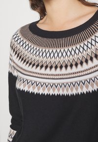 Svart stickad tröja med en texturerad okdel med geometriska mönster i vitt, beige och svart. Rundad halslinning med ribbat kanten.