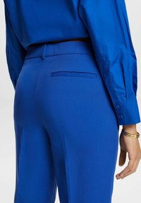 Modré kalhoty na míru s hladkým povrchem, s zadní kapsou a slim fit střihem. Nosené s odpovídající modrou košilí.