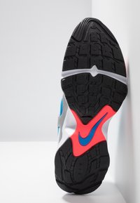 La semelle de la chaussure Nike est en caoutchouc noir avec des deep treads, des accents bleu vif et une section rouge. Le design comprend des motifs texturés pour une meilleure adhérence.