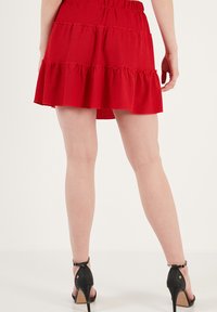 Punat kerah merah terbuat dari kain teksur, dengan pinggang elastis dan hem berenda. Dipadukan dengan sandal bertumit tinggi hitam yang bersandang.