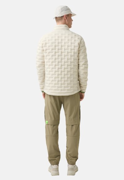 Light beige quilted puffer jacket with high collar, paired with olive green cargo pants featuring pockets and a neon green logo tag.