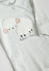 Salopetă în dungi gri și alb cu un design pufos, brodat, reprezentând o oaie și textul "baa-baa." Are capse pentru o îmbrăcare ușoară.