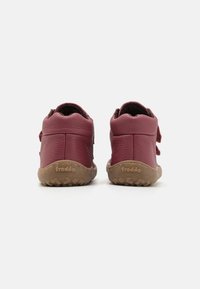 Pantofi din piele burgundă cu suprafață texturată, talpi flexibile din cauciuc maro și închideri cu arici, având călcâie deschise și logo-ul mărcii.