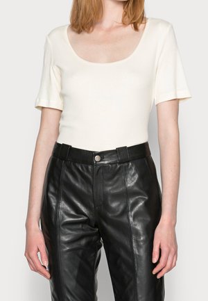 Kremowa bluzka z krótkim rękawem i okrągłym dekoltem, zestawiona z czarnymi, skórzanymi spodniami o wysokim stanie, z widocznym guzikiem i gładką teksturą.