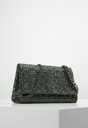 Donkergroene rechthoekige clutch met pailletten over het hele oppervlak en een zilveren kettingriem, rustend op een wit voetstuk tegen een effen achtergrond.