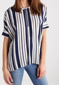 Blouse à manches courtes rayée bleu marine et blanc, avec un col rond et un motif vertical élégant ; tissu léger avec une coupe ample.