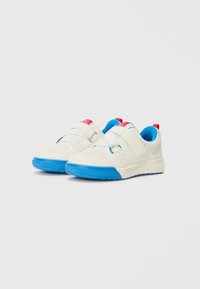 White sneakers with blue outsole and accents, featuring a textured upper, hook-and-loop straps, and red branding detail on the heel.