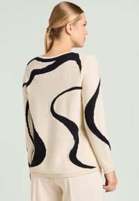 Maglione crema con motivo a onde astratte nere, polsini e orlo a coste. Tessuto morbido con sottili macchioline sparse.