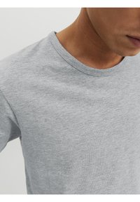 Gros plan sur une personne portant un t-shirt à col rond léger gris uni, montrant le col et une partie du visage.