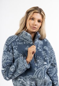 Fleece-pullover i blå med en struktureret overflade og svirvelmønster. Har en halvlodhals og lange ærmer med ribbede manchetter.