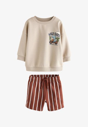 Beige langærmet skjorte med en tegneserie krokodille på en motorcykel og "Wild Days" tekst, kombineret med brune stribede shorts med elastik i taljen.