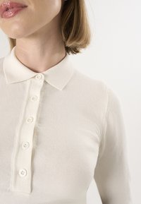 Langærmet polo i cremefarvet med tekstureret stof, klassisk krave og en knapliste med fem små knapper.