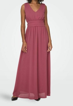 Woman wearing sleeveless, deep rose, floor-length dress with V-neckline and fitted waistband, standing on white background.