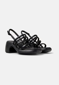 Black heeled sandals with multiple intersecting straps, a textured block heel, and a cushioned black sole. Adjustable slingback design.