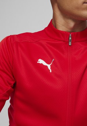 Rode zip-up jas van gestructureerde stof, met een hoge kraag en een wit Puma-logo op de borst.