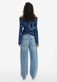 Blaues schulterfreies Oberteil aus strukturiertem Stoff mit langen Ärmeln, kombiniert mit oversized hellblauen Jeans aus Denim mit lockerem Schnitt und Gesäßtaschen.