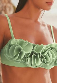 Mintgrön bikiniöverdel med spaghettiarmband, med lager av volanger över framsidan, tillverkad av mjukt, strukturerat material.