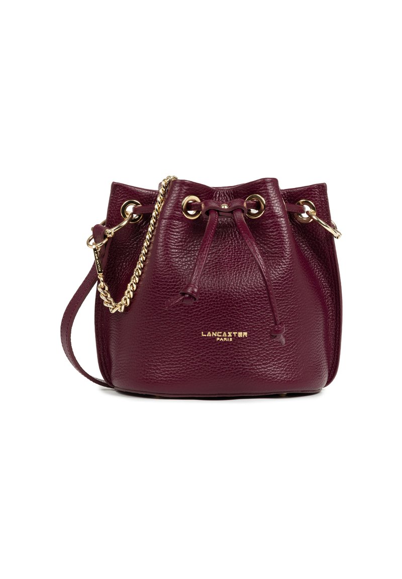 Sac en cuir bordeaux en forme de seau avec une finition texturée, œillets dorés, fermeture à cordon et une bandoulière en chaîne tissée. Présente le logo de la marque en doré.