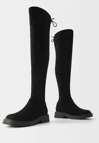 Svarta stövlar i mocka som går över knäna, med rund tå, platt sula och bakre snörning för justering av passform. Slät textur genom hela stöveln.