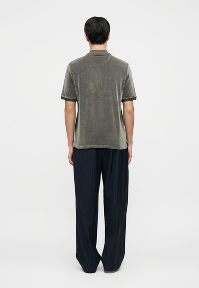 Πόλο πουκάμισο σε ελιά πράσινο με κοντά μανίκια, με μαύρες αντίθετες μανσέτες και άνετη εφαρμογή, συνδυασμένο με φαρδιά παντελόνια με ναυτικά ριγέ.