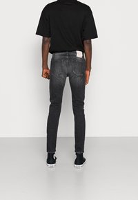 Hubené černé džíny s vybledlým povrchem, obsahující etiketu na zadním díle a dvě zadní kapsy. Nosit s černými teniskami.