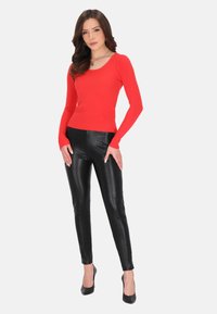 Rode geribbelde longsleeve top gecombineerd met zwarte lerenachtige aansluitende broek en zwarte hoge hakken, voor een witte achtergrond.