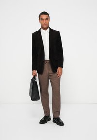 Svart sammet blazer, vit skjorta, bruna texturerade byxor och svarta läderskor. Bär en svart läder tote-väska. Enkel, modern design.