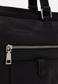 Černá kožená taška s kovovým zipem, texturovaným materiálem a magnetickým uzávěrem. Obsahuje detailní švy a kovové akcenty.