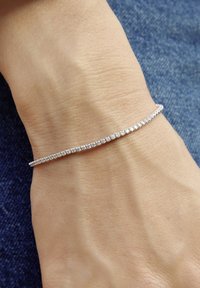 Delicada pulsera de plata con pequeñas piedras transparentes llevada en una muñeca sobre un fondo de tela azul.