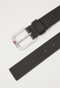 Ceinture en cuir noir avec une boucle rectangulaire en argent. Boucle gravée avec "TOMMY JEANS". Comprend trois trous de ceinture et des coutures le long du passant.