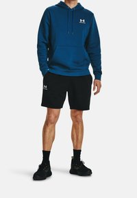 Sweatshirt à capuche bleu avec une poche avant et des cordons, porté avec un short noir et des chaussures de sport noires avec des semelles texturées.