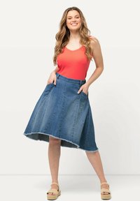 Falda de mezclilla con un dobladillo asimétrico y bolsillos laterales, combinada con una camiseta sin mangas roja brillante. La tela es suave con un borde ligeramente deshilachado.