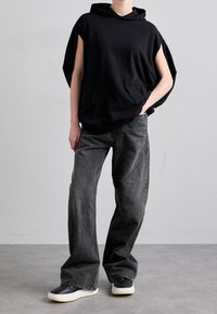 Svart oversize hoodie med korta ärmar, utrustad med en framficka, matchad med mörkgrå vida jeans och svarta sneakers med vit sula.