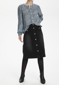 Blå mønstret bluse med knaplukning, lange ærmer og høj-lav kant, parret med en sort denimnederdel med høj talje og knapper. Sorte ankelstøvler.