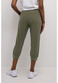 Olijfgroene cropped broeken van zacht stof, met een elastische taille en strakke boorden. Draagt met witte sneakers. Eenvoudig, casual ontwerp.