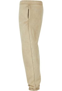Beige sweatpants laget av myk tekstil, med snor i livet, sidelommer og ribbede cuff-er. Glatt overflate med en subtil glans.
