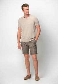 Beige short-sleeve polo shirt with a v-neck and textured fabric, paired with brown linen shorts and light brown slip-on shoes.
