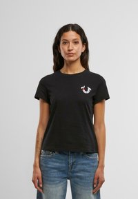 Must musta crew-neck t-särk lühikeste varrukatega, millel on rinnal punane ja valge tikand. Lõdva istuvusega.
